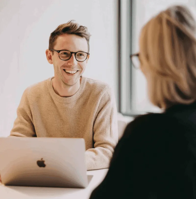 Smilende kundeservicemedarbejder arbejder på bærbar computer under møde — Digital Asset Management (DAM) og Product Information Management (PIM) løsninger fra Kontainer.