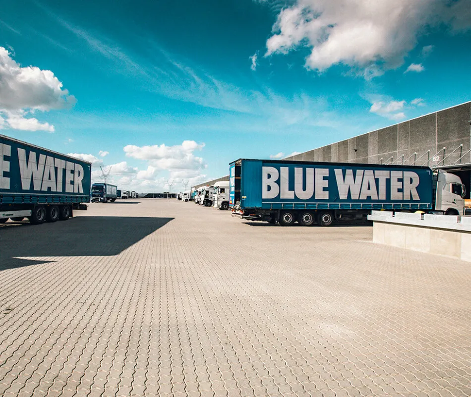 Kontainer DAM_Blue Water Case_Trucks Blue Water trucks outside a warehouse under a blue sky.